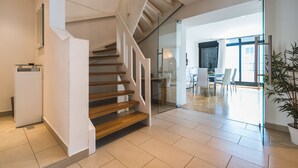 Een modern interieur met een houten trap, een glazen deur naar een eethoek, en een kamerplant.