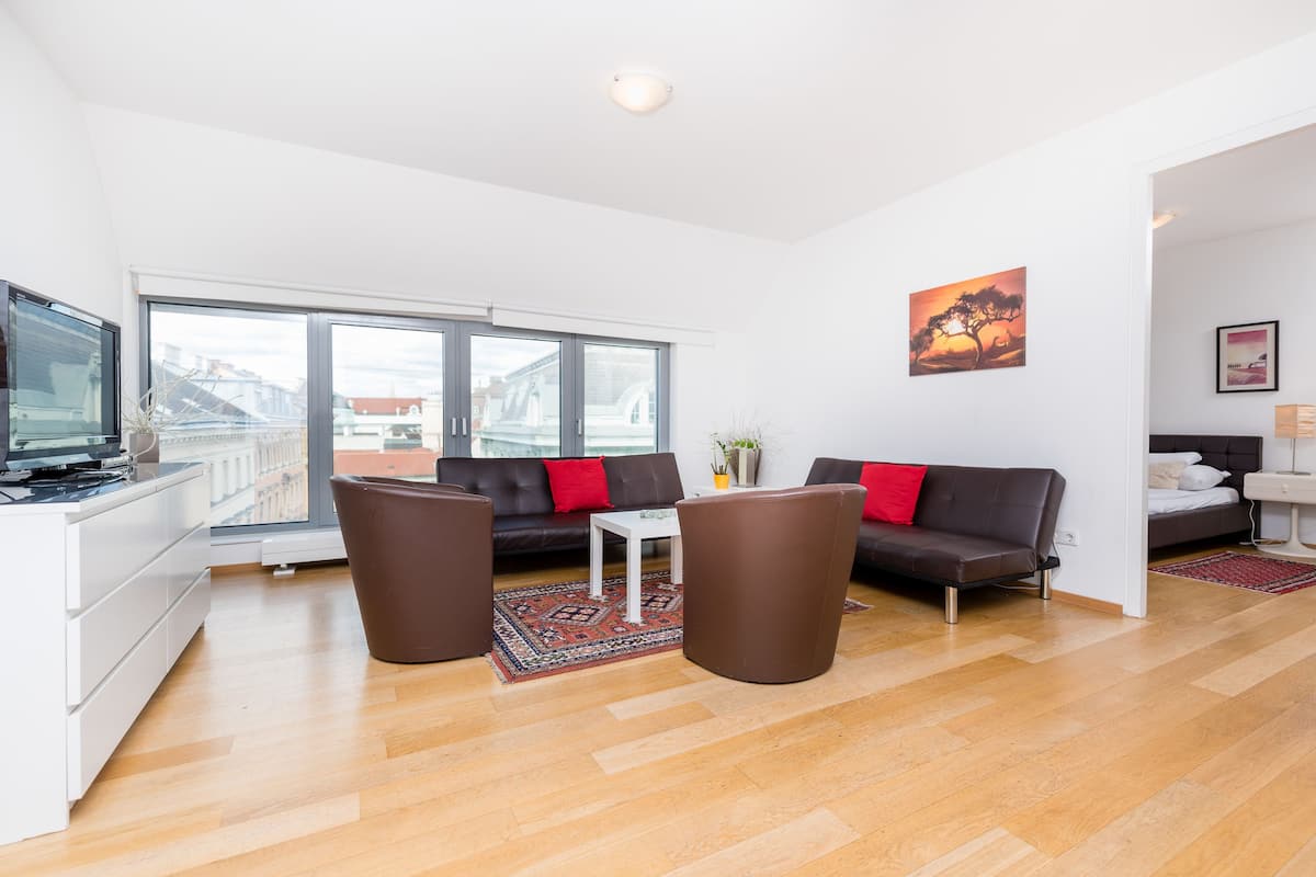 A modern living room with a sofa, two chairs, a coffee table, and a TV.