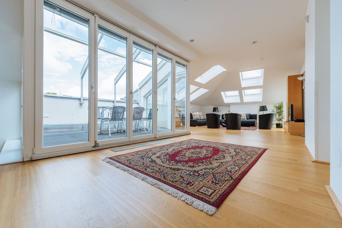 A spacious living area with a large sliding glass door leading to a balcony, a patterned rug, and a modern interior design.