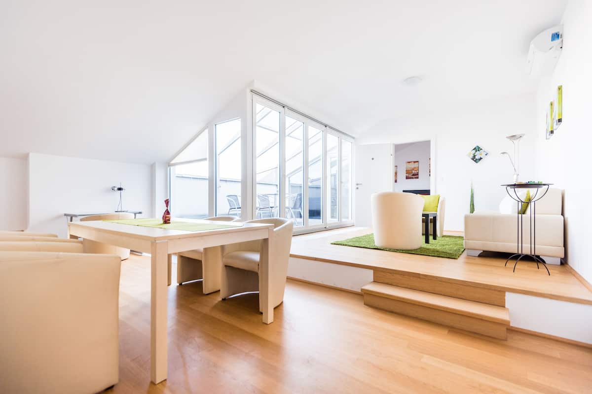 A modern living room with a large window, a dining table, and a sofa.
