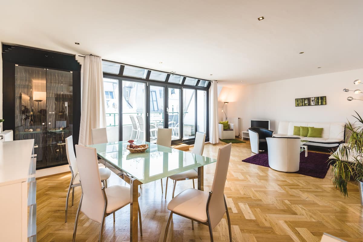 A modern living room with a glass dining table, white chairs, a sofa, and a TV.