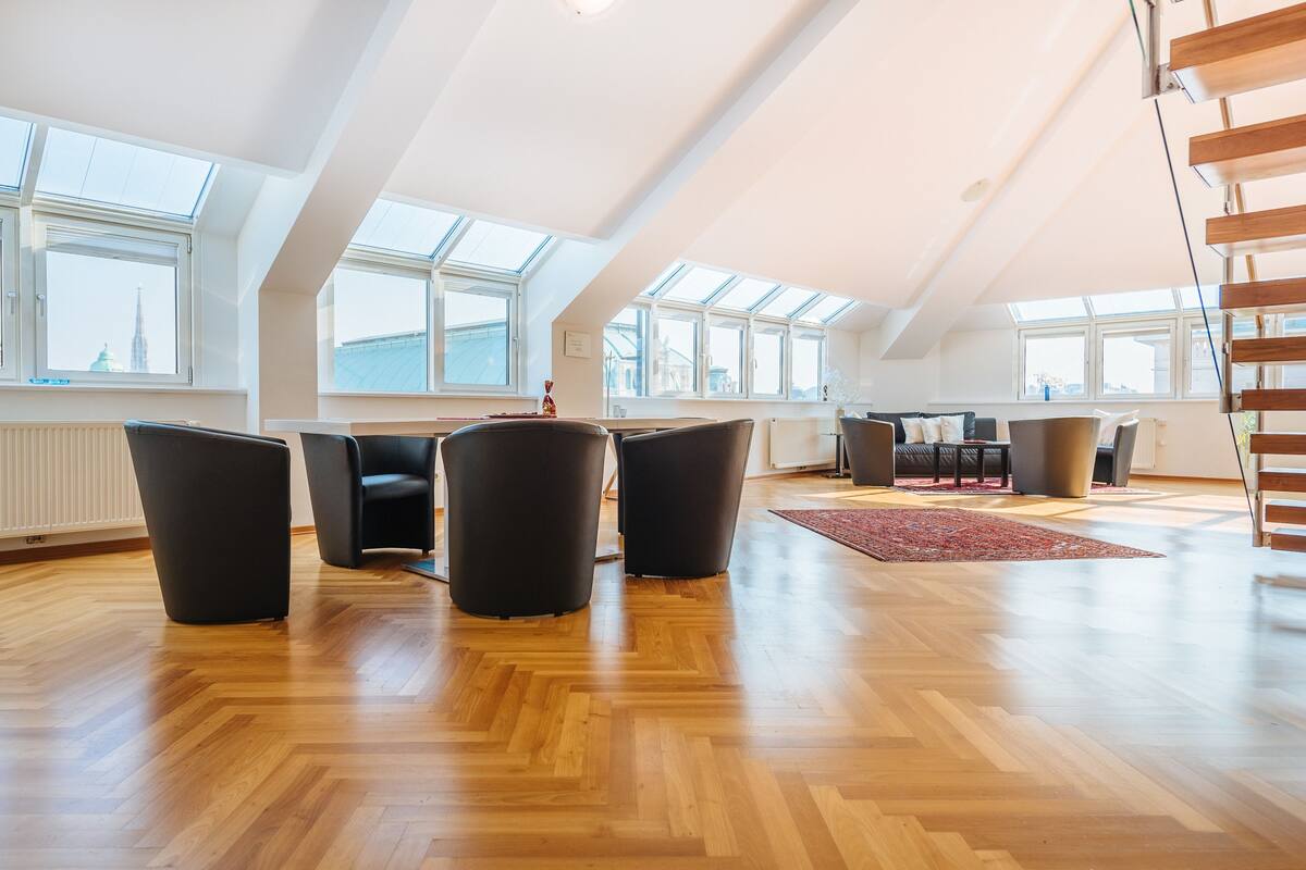 A spacious loft apartment with a high ceiling, large windows, and a wooden floor.