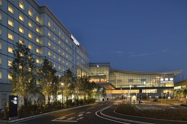 A modern hotel with a curved glass facade, multiple floors, and a well-lit entrance area.