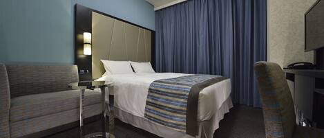 A hotel room with a bed, a sofa, a desk, and a television.