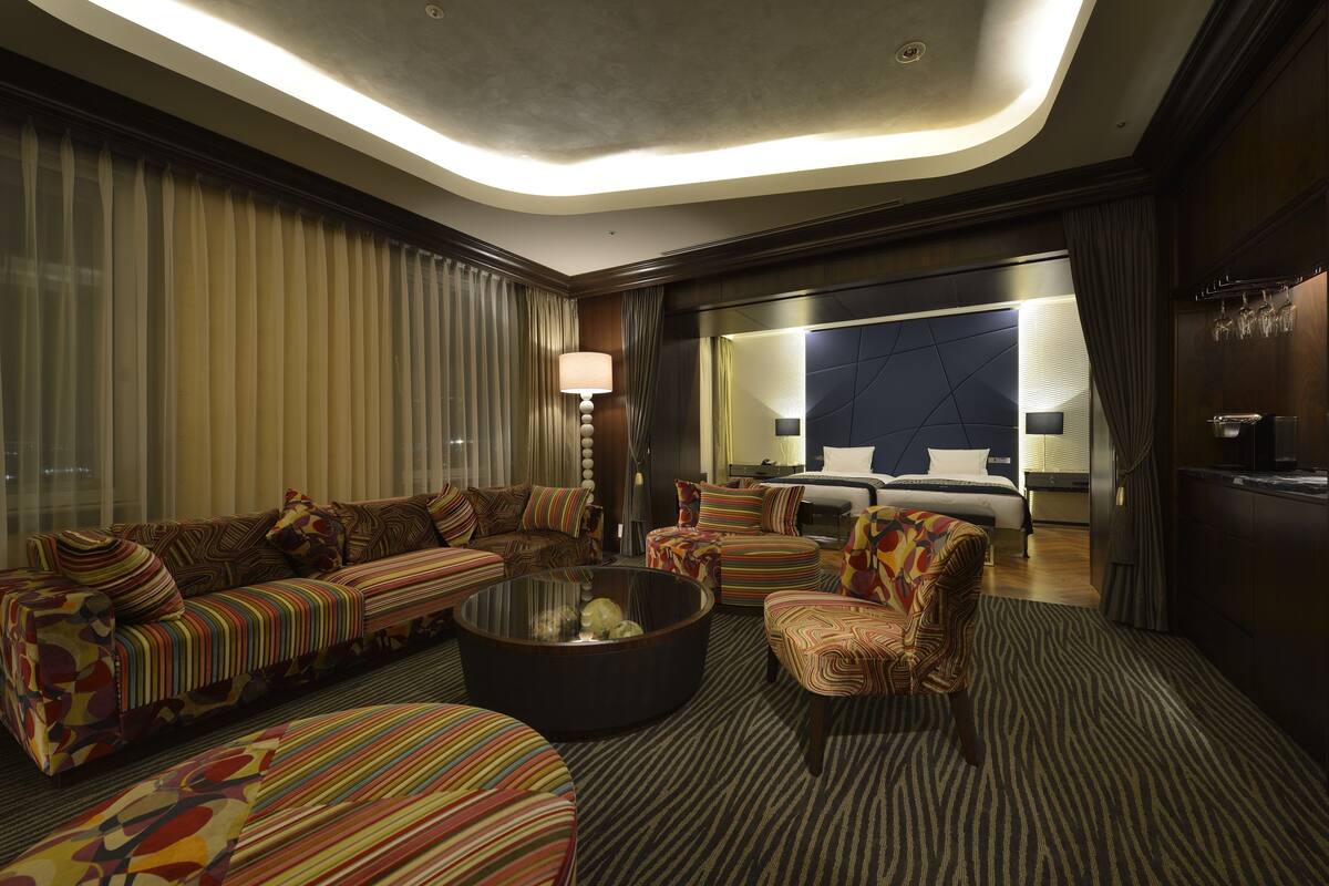 Una habitación de hotel moderna con un conjunto de sofá, una mesa de centro redonda y una cama con cabecero.
