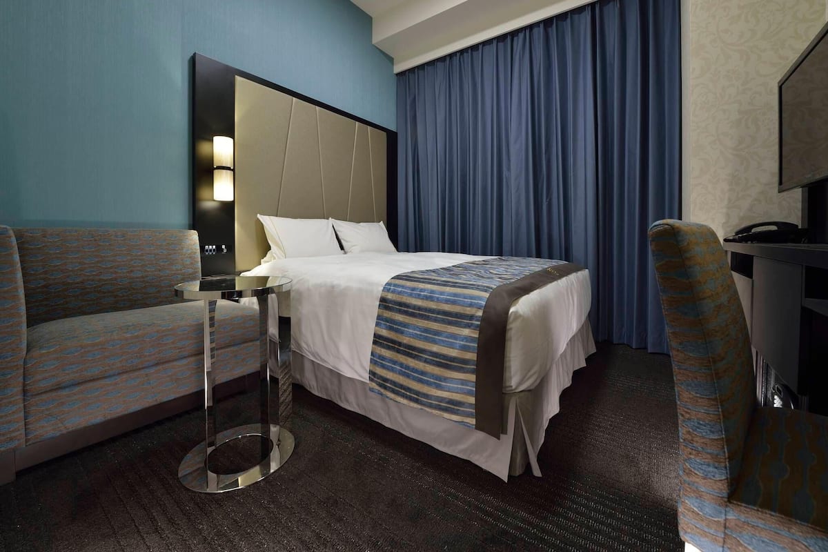 A hotel room with a bed, a desk, a chair, and a TV.