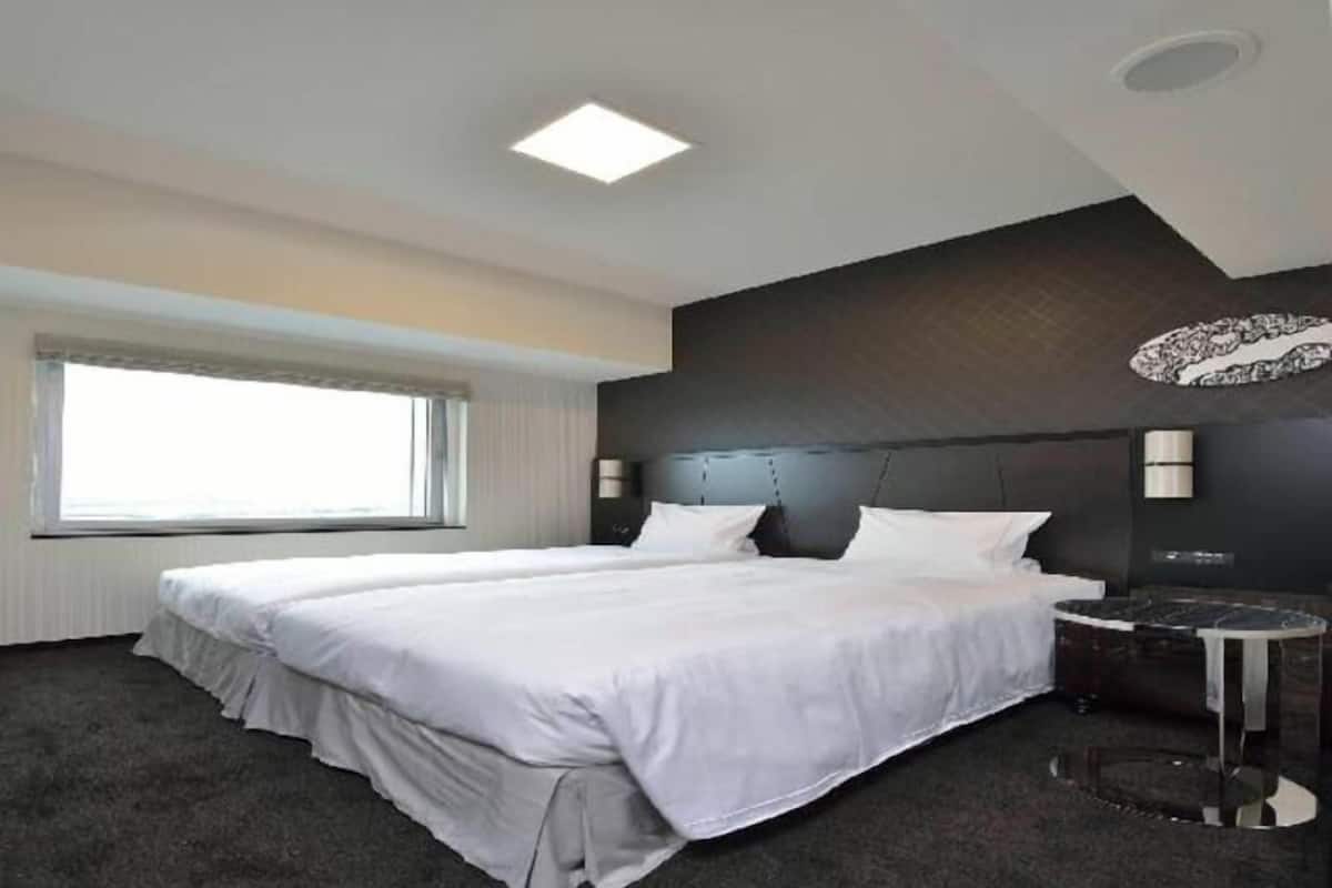 Une chambre d’hôtel moderne avec un grand lit, une petite table ronde et une grande fenêtre.