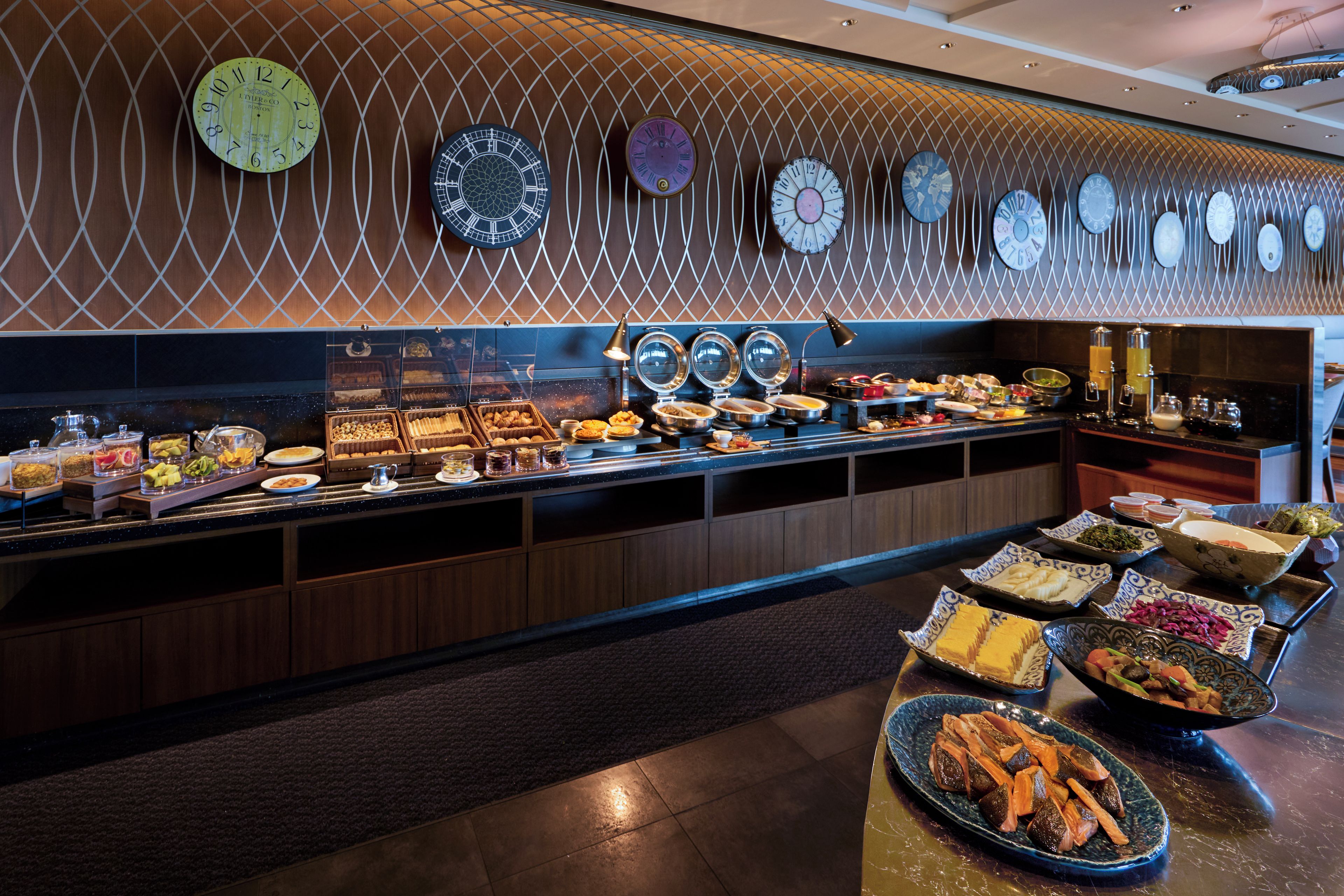 Un buffet proposant une variété de plats et un mur orné de nombreuses horloges.