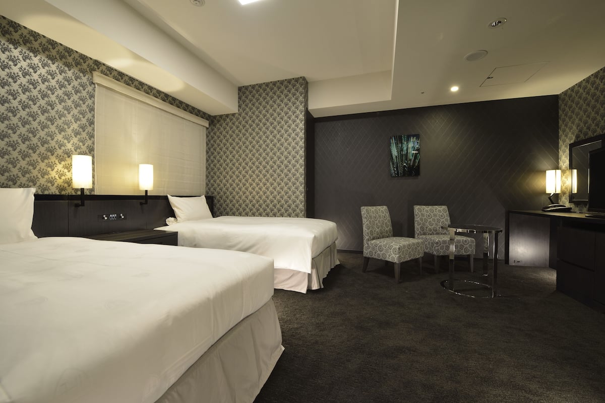 Une chambre d’hôtel avec deux lits, un bureau, une chaise et un téléviseur.