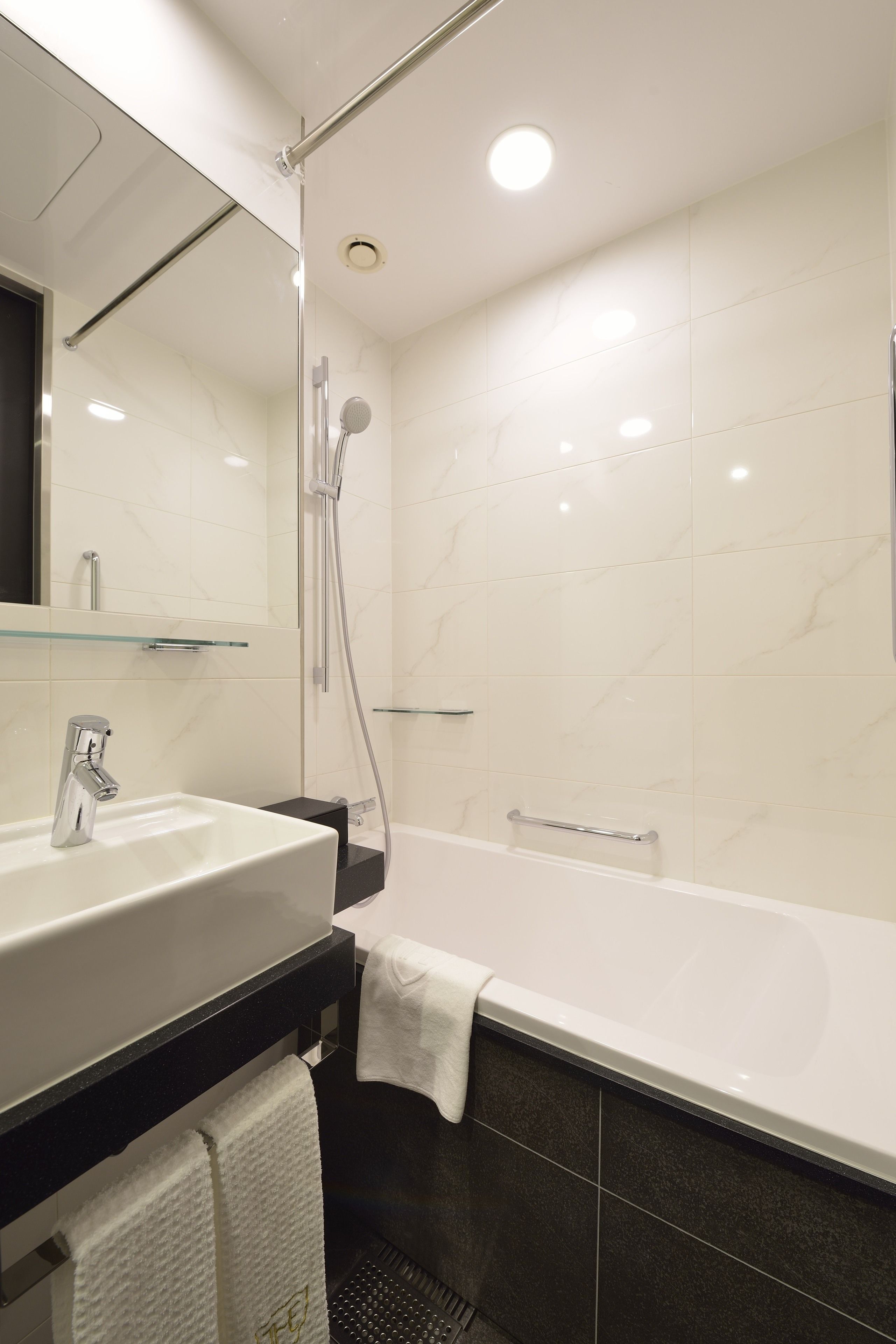 A modern bathroom with a white sink, a glass shelf, a bathtub, and a shower.