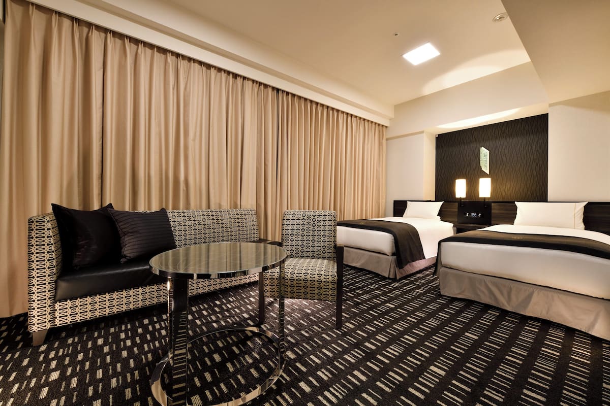 Une chambre d’hôtel avec un canapé, un fauteuil, une petite table, un lit et un sol recouvert de moquette.
