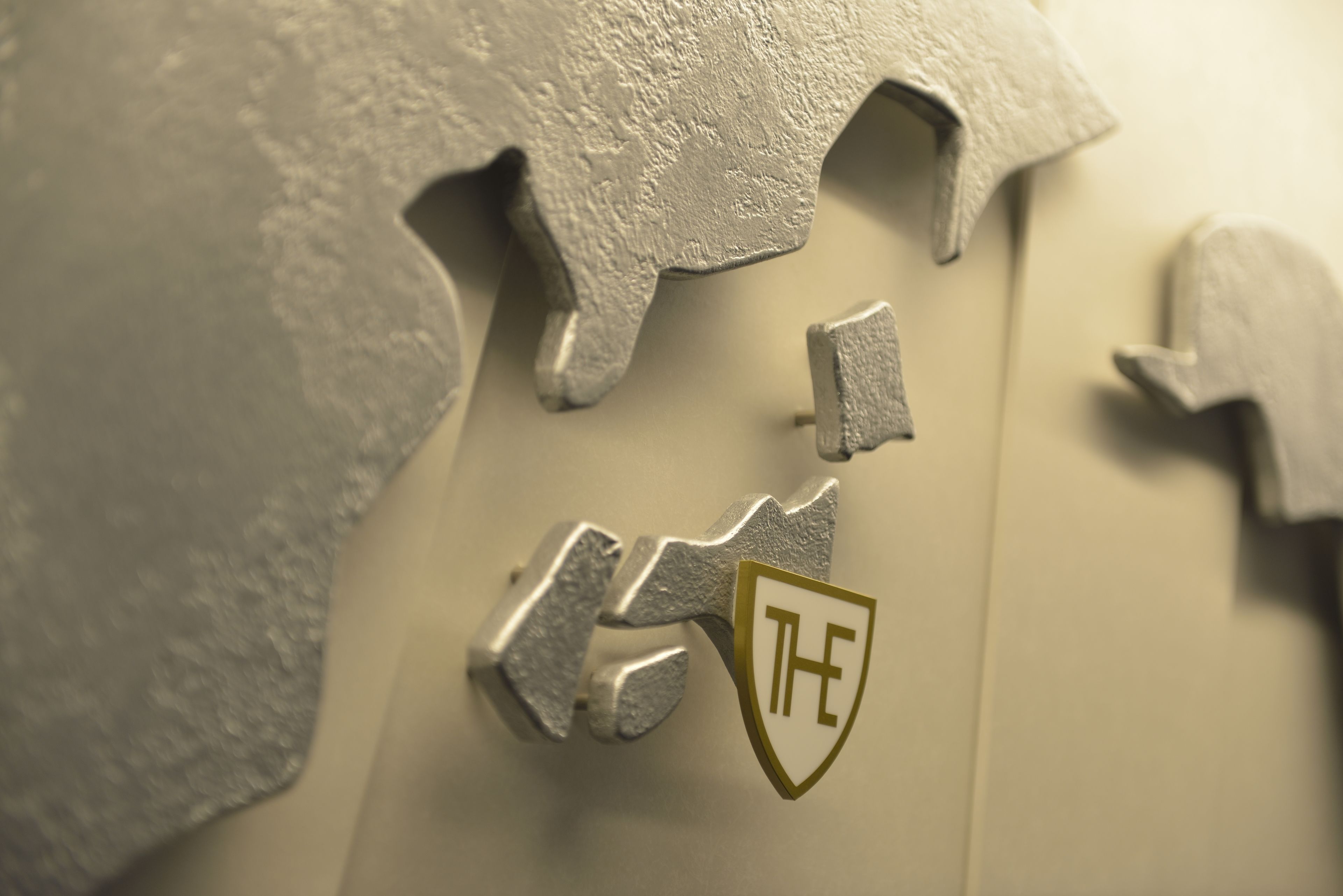Primer plano de un emblema metálico con las letras “TH” sobre una superficie texturizada.