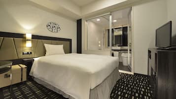A hotel room with a large bed, a bedside table, a TV, a bathroom with a toilet and sink, and a mirror.