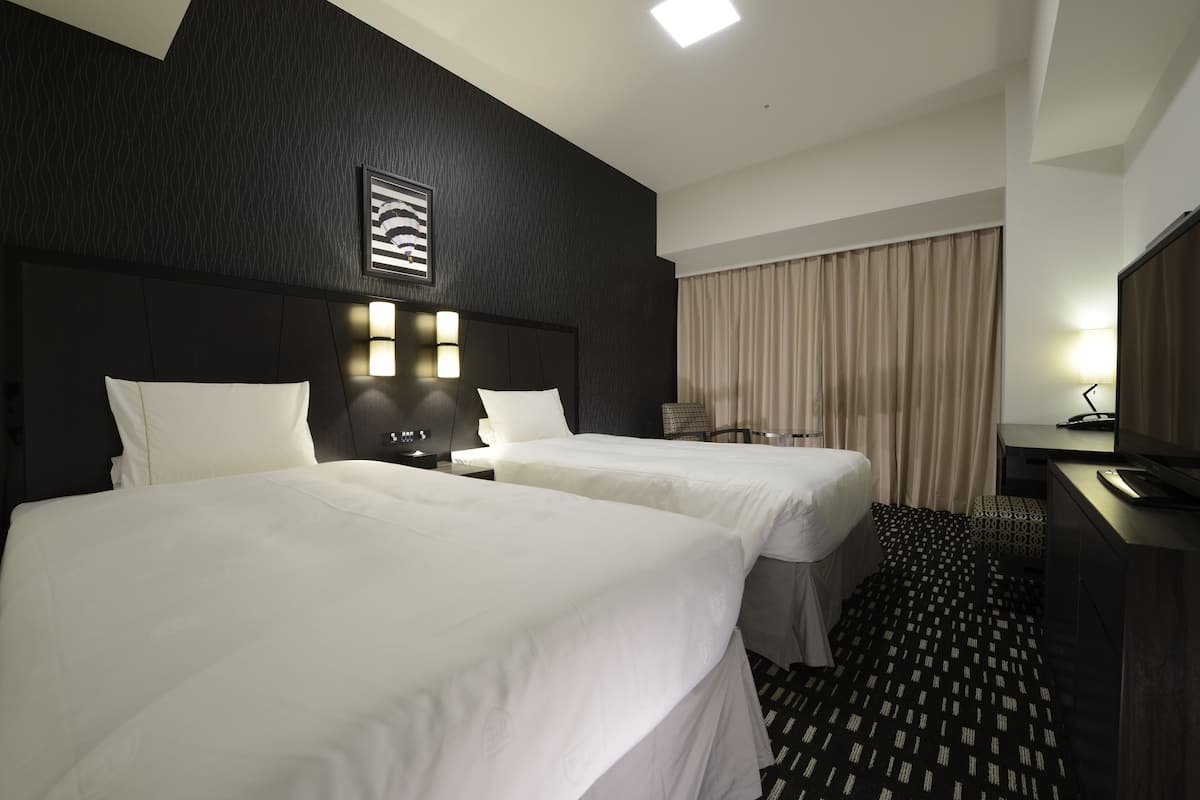 Une chambre d’hôtel avec deux lits, un bureau, une chaise, une télévision et une fenêtre avec des rideaux.