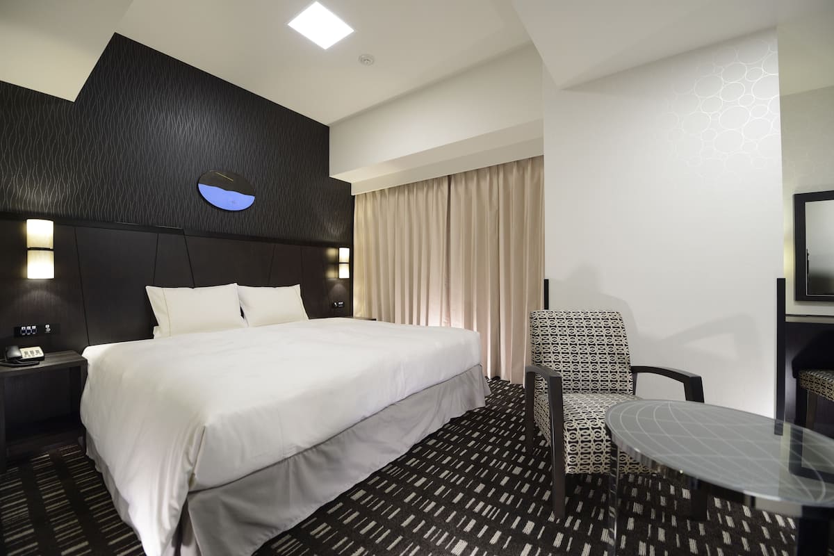 Une chambre d’hôtel avec un grand lit, un bureau avec une chaise, une petite table et un téléviseur fixé au mur.