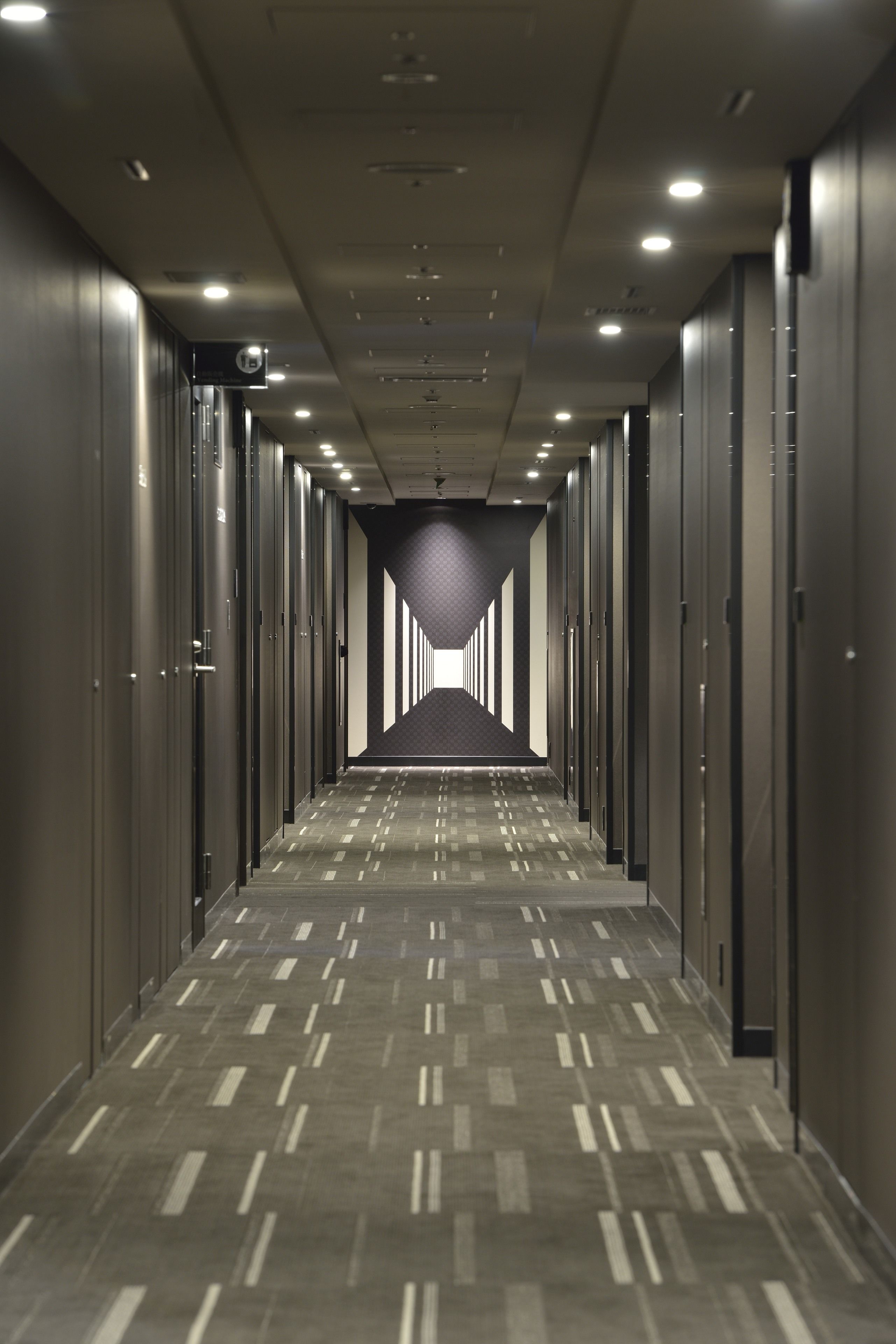 A long, narrow hallway with rows of closed doors on either side, leading to a darkened end.