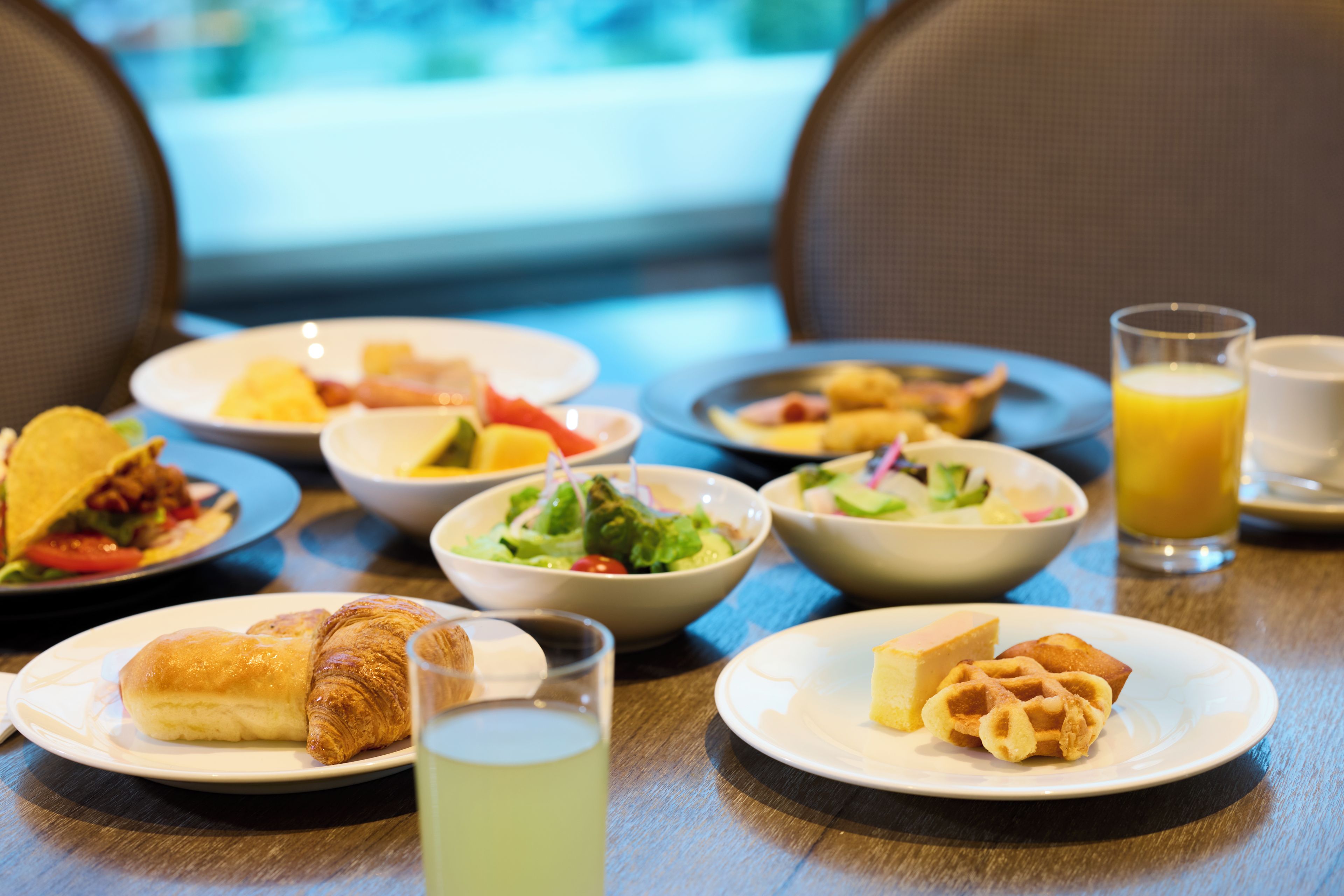 Ein Frühstückstisch mit verschiedenen Speisen, darunter Croissants, Waffeln und Salate.
