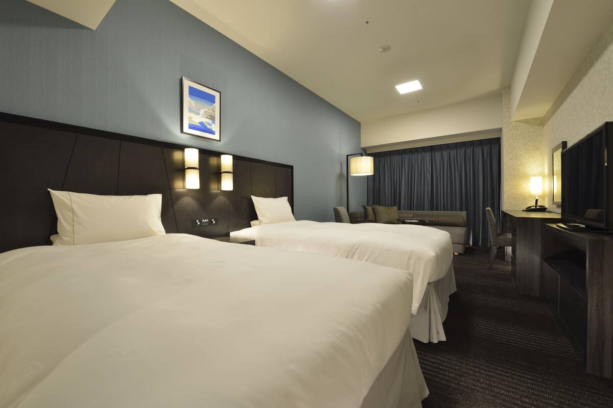 Une chambre d’hôtel avec deux lits, un bureau, une chaise et un téléviseur.
