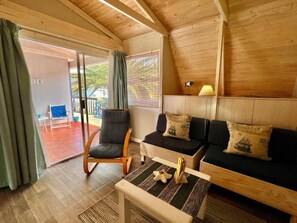 Quarto aconchegante com teto de madeira, sofá, uma poltrona, mesa pequena e luminária.