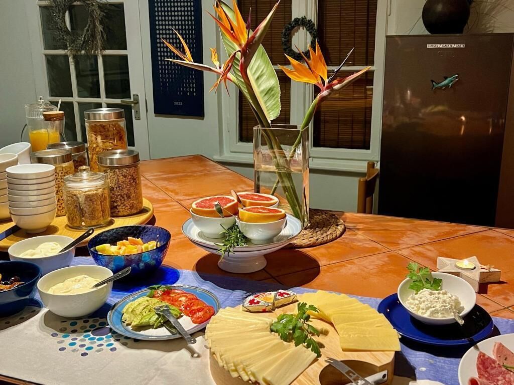 Ein Tisch mit verschiedenen Speisen und Beilagen, darunter Käse, Brot und einer dekorativen Pflanzengestaltung.