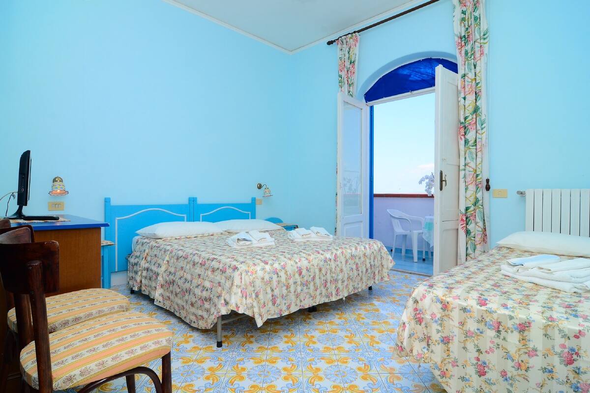 Een kamer met twee bedden, een bureau en een stoel. Er is een raam met gordijnen en uitzicht op het omliggende landschap.