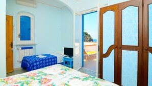 Une chambre à coucher avec un lit, une télévision, une petite table et une vue sur la plage par une porte ouverte.
