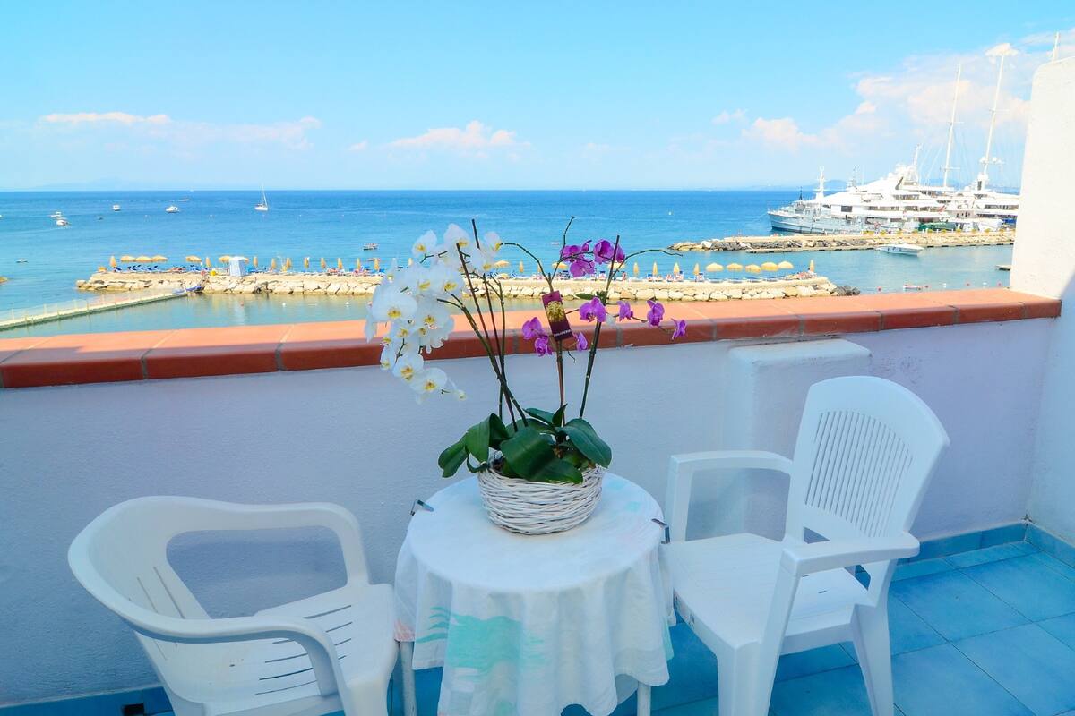 Een balkon met uitzicht op zee, met een tafel, stoelen en een bloempot.
