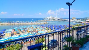 Un port de plaisance avec de nombreux bateaux, un grand yacht et une zone de plage équipée de parasols et de chaises longues.