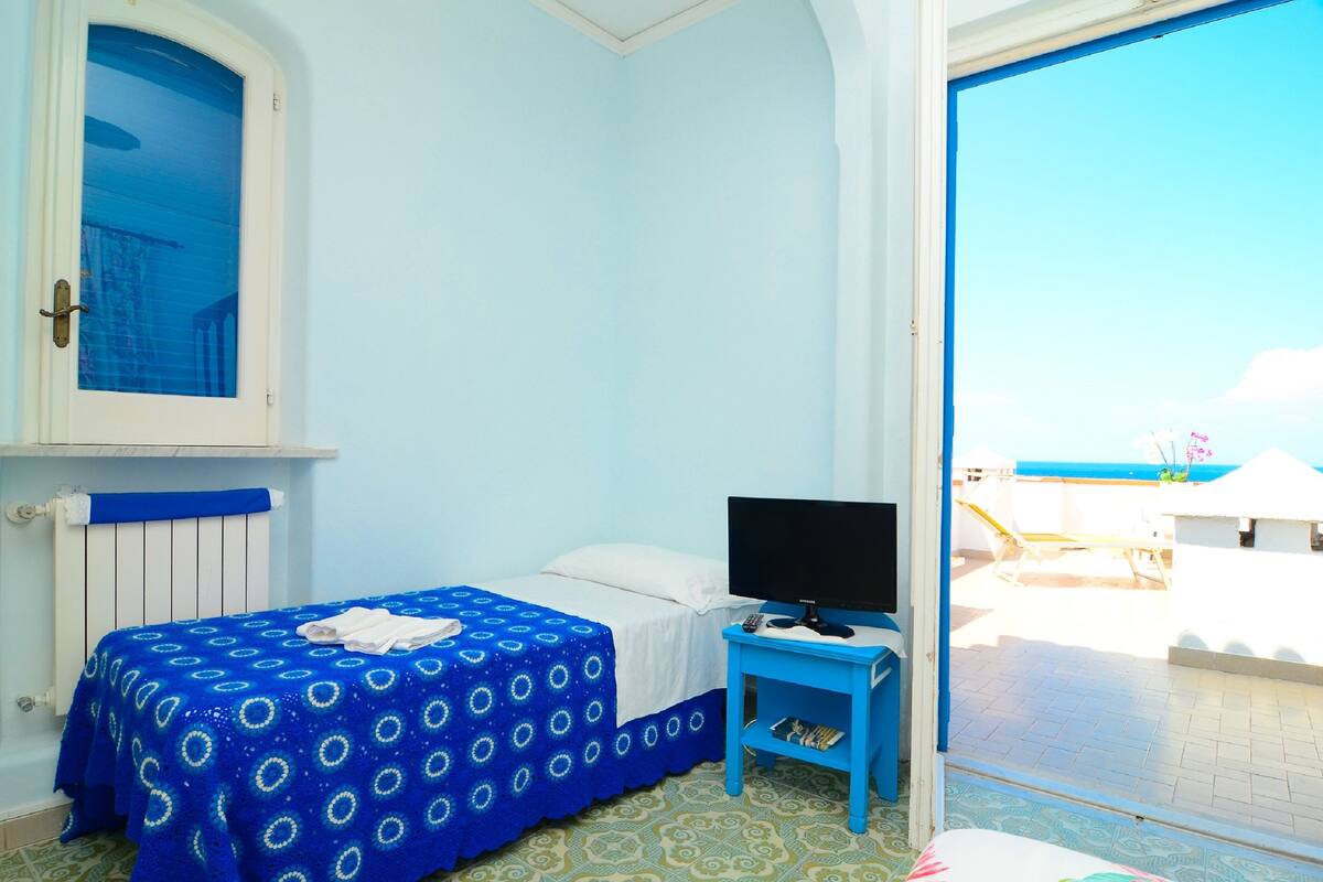 Een kamer met een bed, een televisie op een tafeltje en uitzicht op zee.