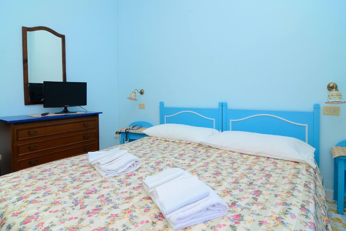 Een slaapkamer met een bed, een dressoir, een televisie en een nachtkastje.