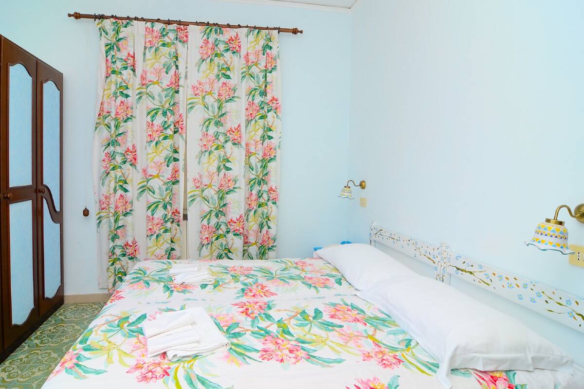Een slaapkamer met een bloemenbedekking, een houten garderobe en een wandlamp.