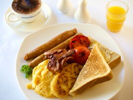 Un plato de comida para el desayuno con huevos, tocino, salchichas, tostadas y tomate.