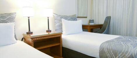 Una habitación de hotel con dos camas, una mesita de noche con lámparas, un espejo y una silla.
