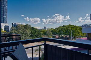 A cityscape with modern buildings, a clear sky, and a view of a road with trees in the foreground.