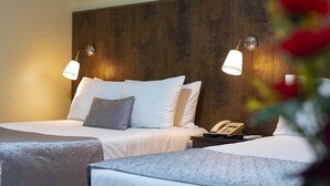 Une chambre d’hôtel avec deux lits, une tête de lit en bois, des lampes de chevet et un téléphone sur une table de chevet.