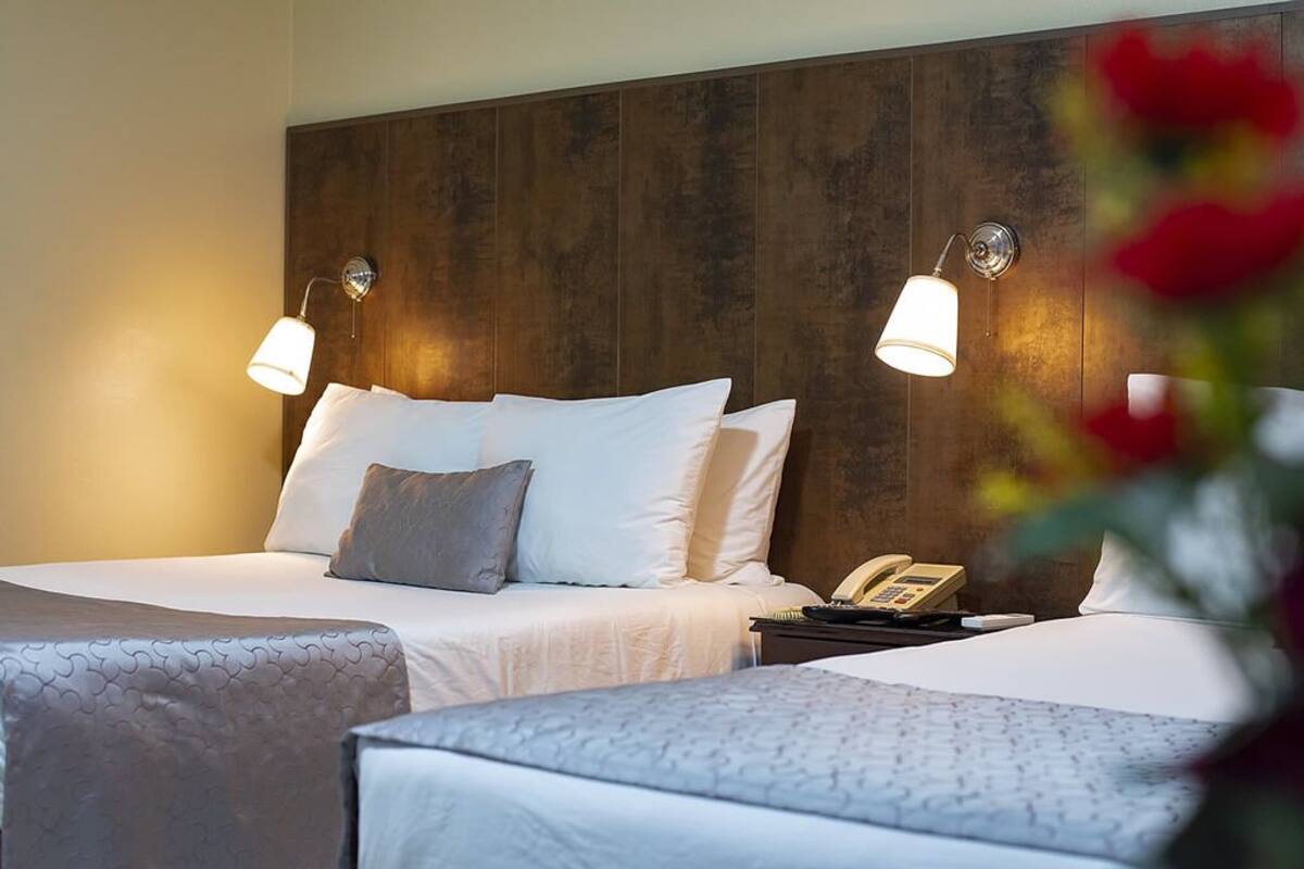 Une chambre d’hôtel avec deux lits, une tête de lit en bois, des lampes de chevet et un téléphone sur une table de chevet.