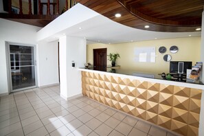 A reception area with a geometric patterned counter, a potted plant, and clocks on the wall.
