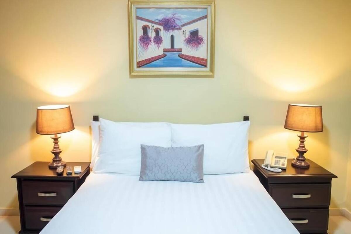 Une chambre d’hôtel avec un lit, deux tables de chevet avec des lampes, un tableau au mur et une petite table de chevet avec un téléphone.