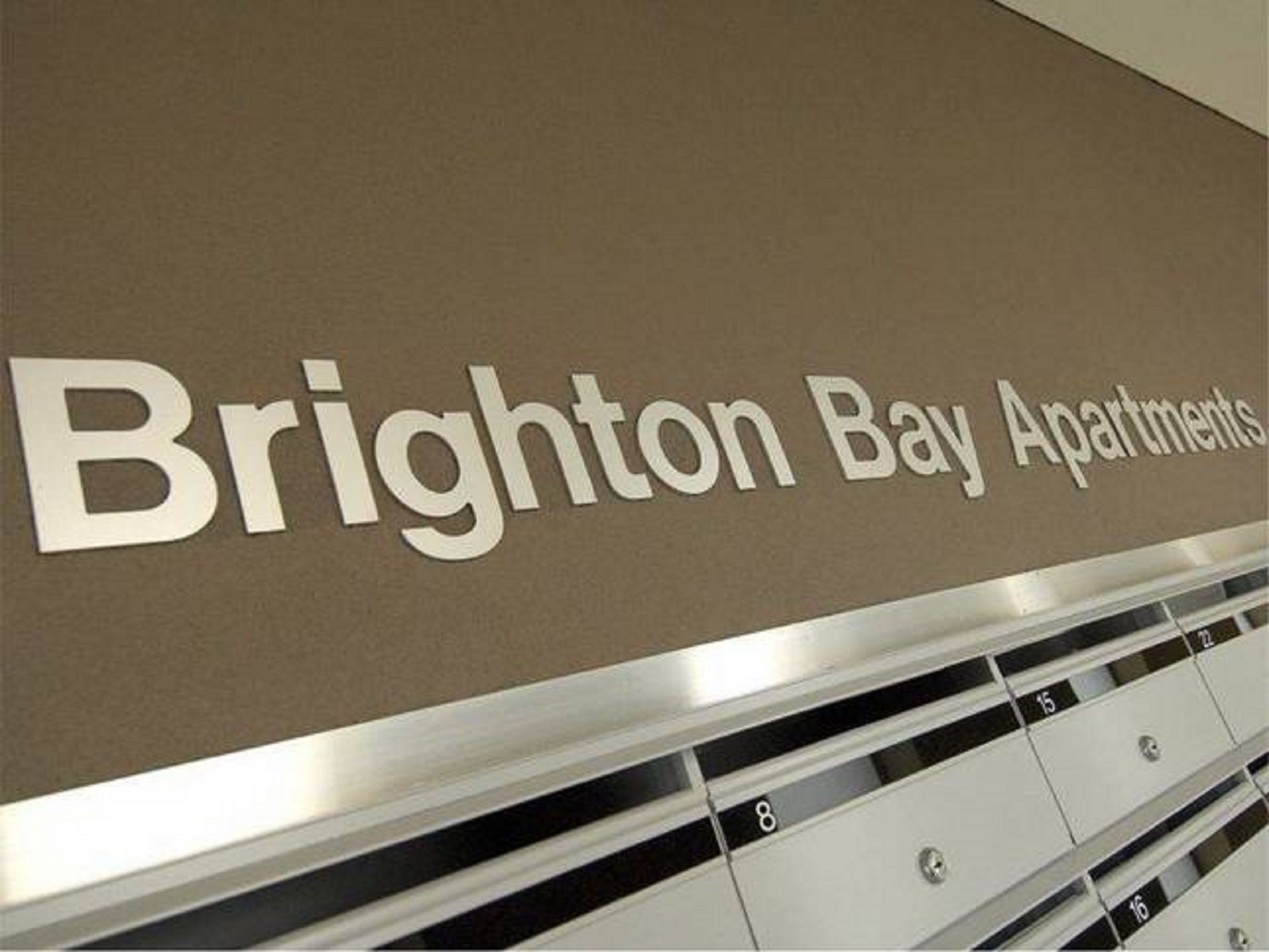 A sign for Brighton Bay Apartments with a row of numbered storage compartments below.