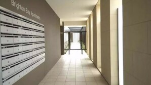 A hallway with a row of mailboxes on the left, leading to a gated entrance. - Brighton Bay Apartments (Brighton)