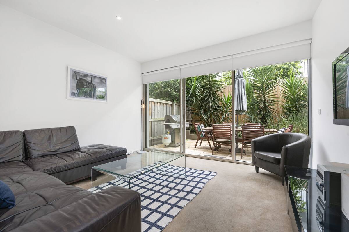 A modern living room with a leather sofa, a glass coffee table, and a view of a patio with a dining area and plants.