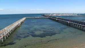 A pier extending into a clear blue sea with a sandy beach at the end. - Brighton Bay Apartments (Brighton)