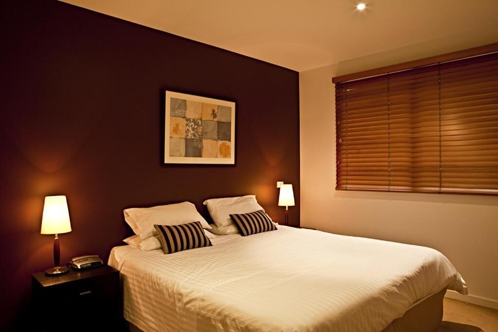 A neatly made bed with a white comforter and striped pillows, a bedside lamp, and a framed artwork on the wall.
