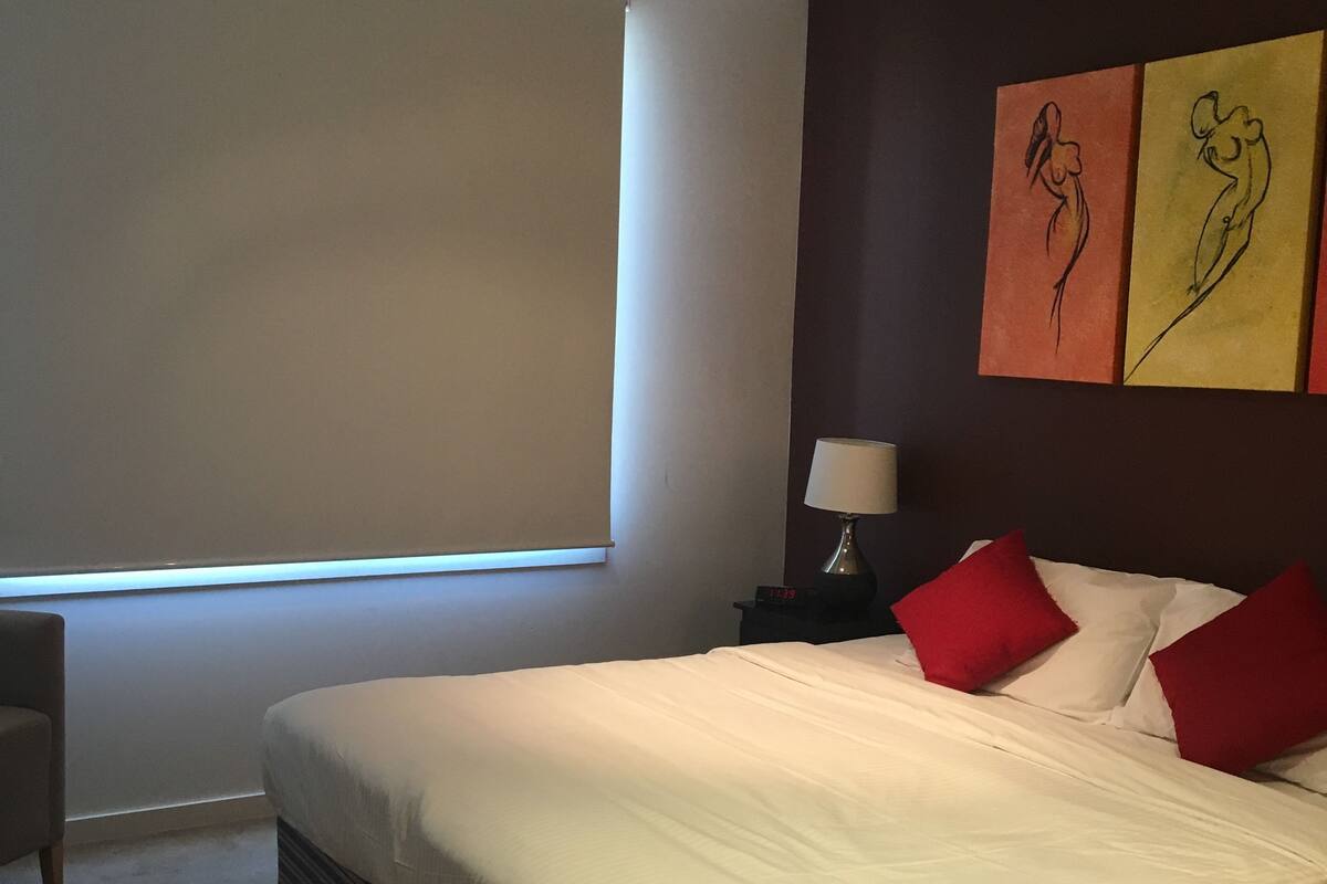 A hotel room with a large bed, a nightstand with a lamp, and artwork on the wall.