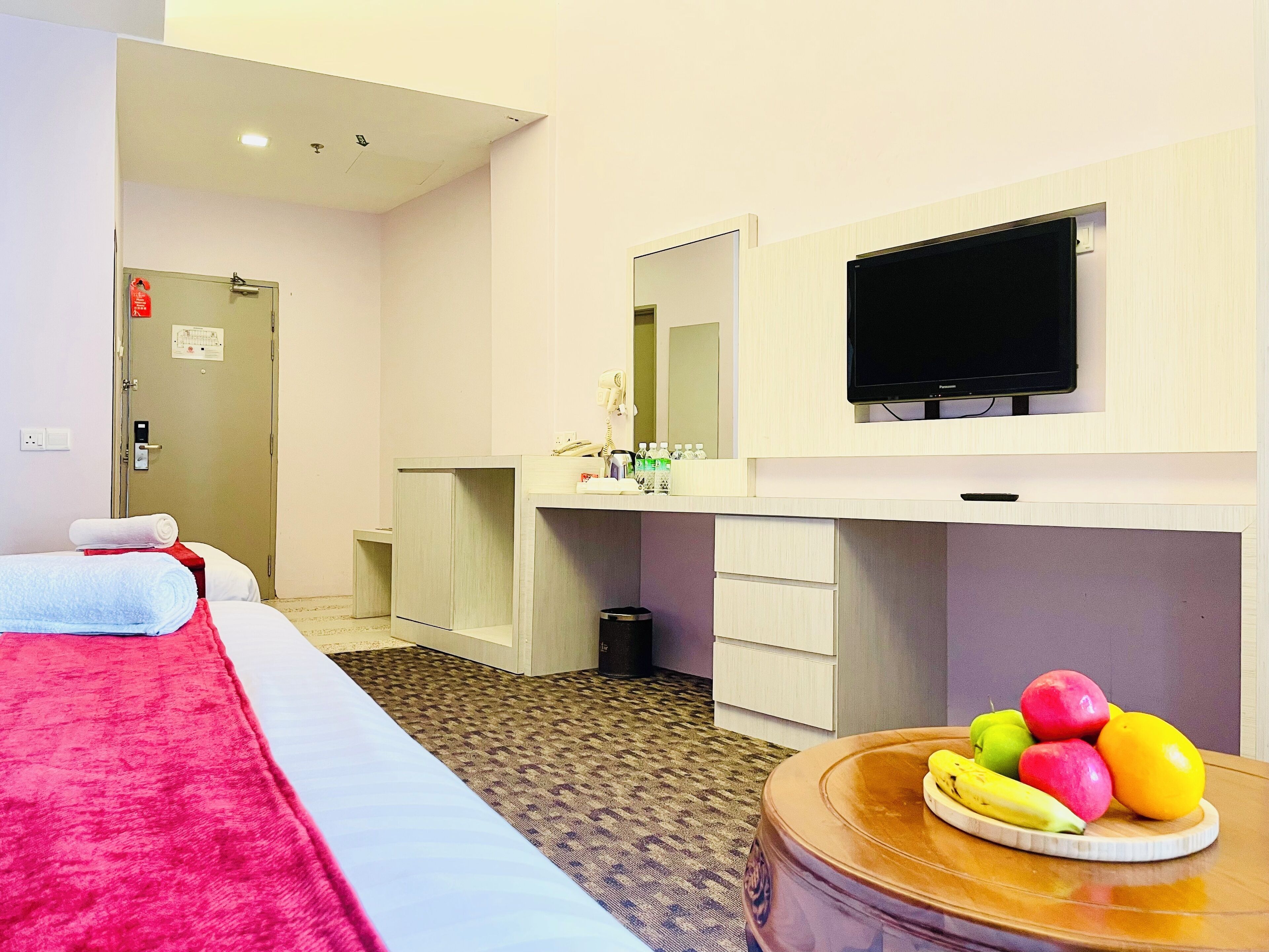 Une chambre d’hôtel avec un lit, un bureau, un miroir, une télévision et un panier de fruits posé sur une table.