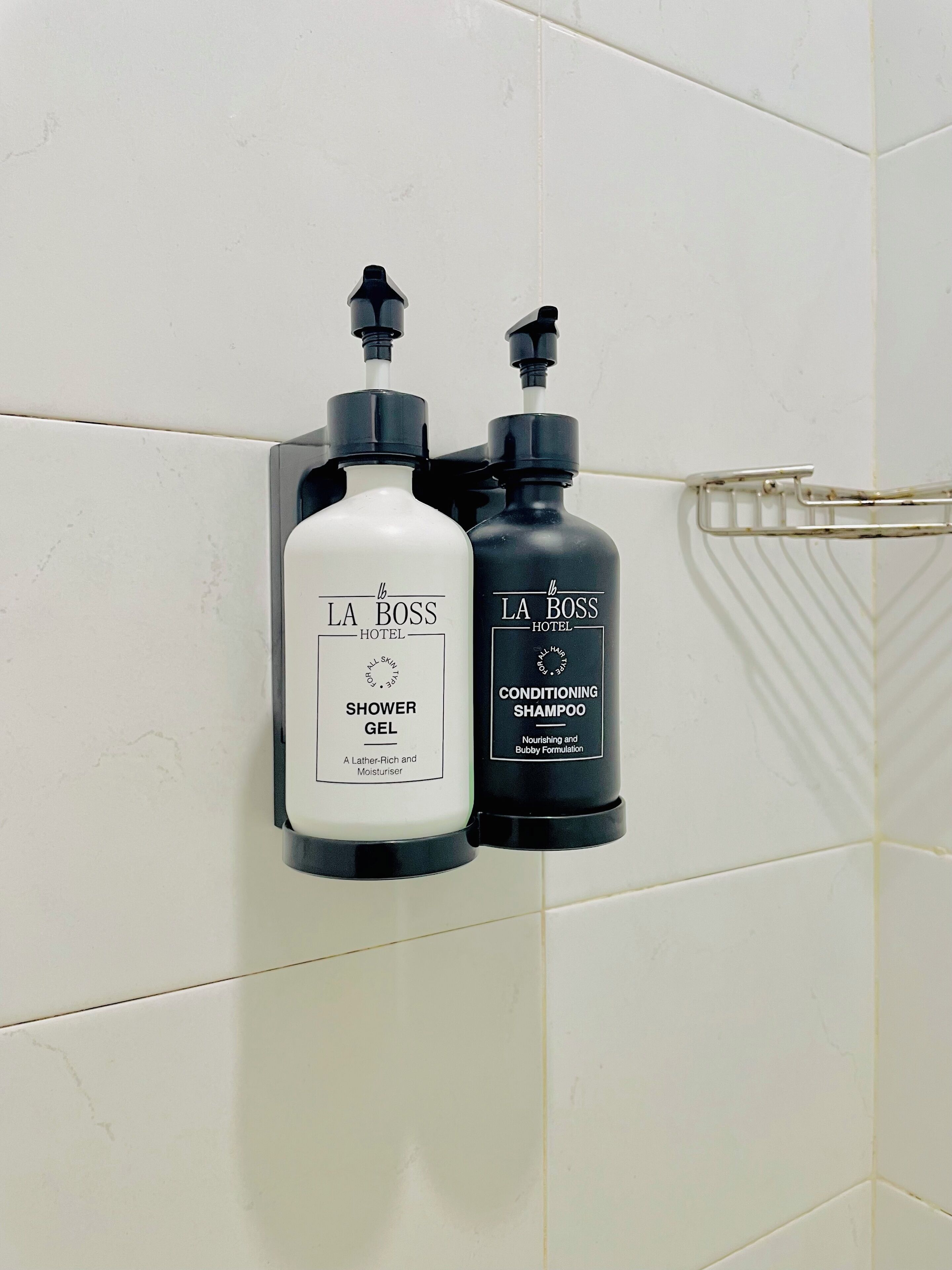 Zwei Flaschen La Boss Hotel Duschgel und Conditioner an einer gefliesten Wand befestigt.