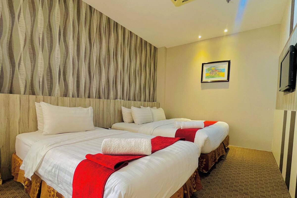 A hotel room with two beds, a wooden headboard, a patterned wall, a framed picture, and a carpeted floor.