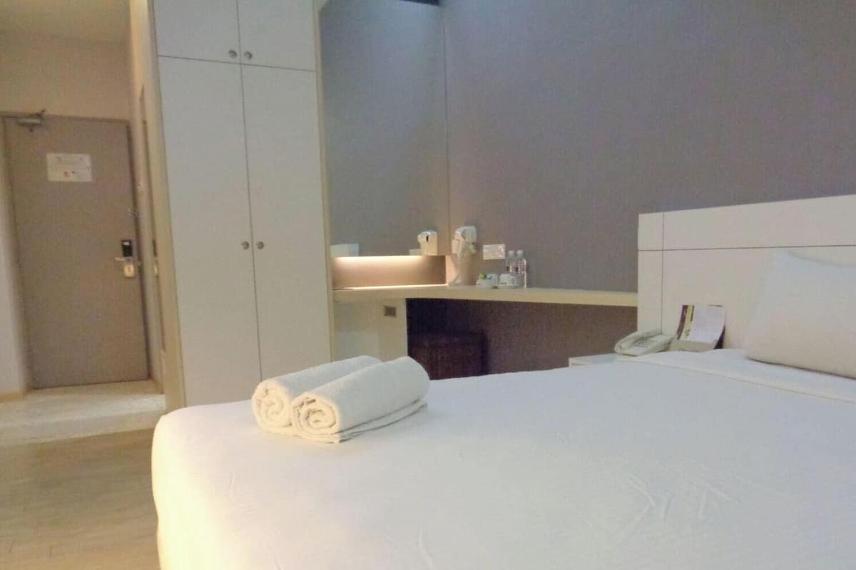 A hotel room with a bed, a bedside table with a phone, a mirror, and a door.