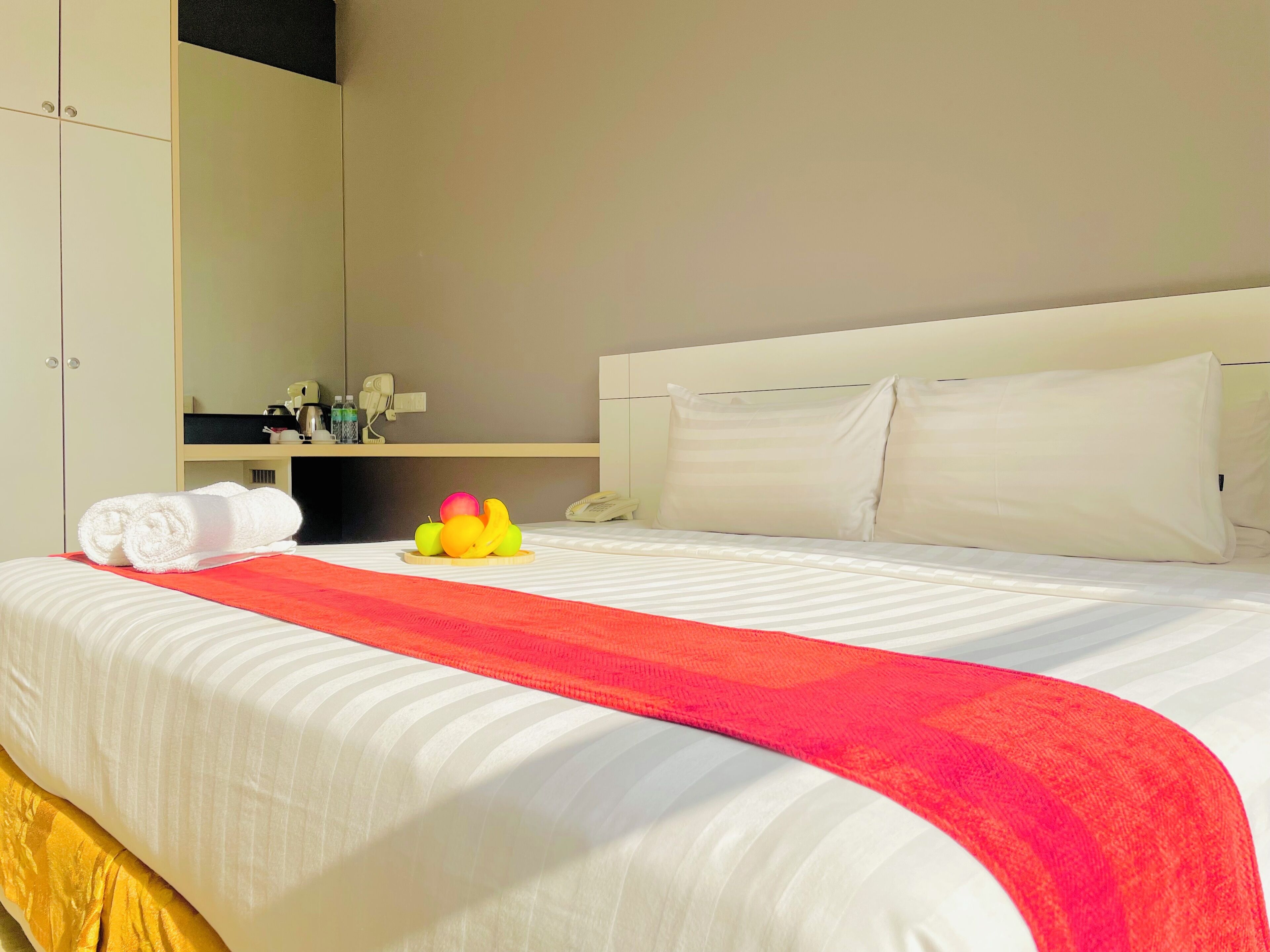 Habitación de hotel con una cama bien hecha, un plaid rojo, un frutero y un minibar.