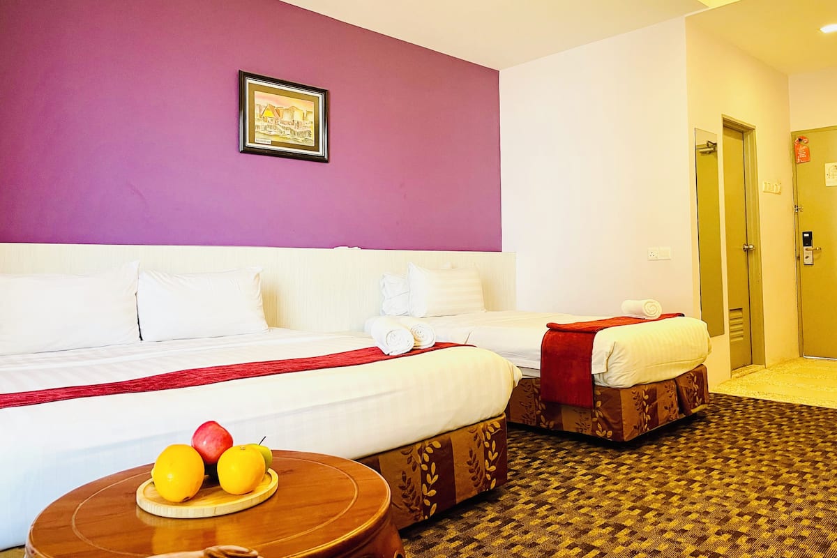 A hotel room with two beds, a framed picture on the wall, and a fruit bowl on a side table.